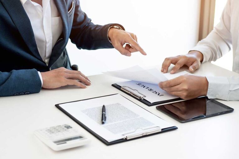 Driver reviews an auto insurance policy beside a parked car while comparing deductible amounts and repair costs.